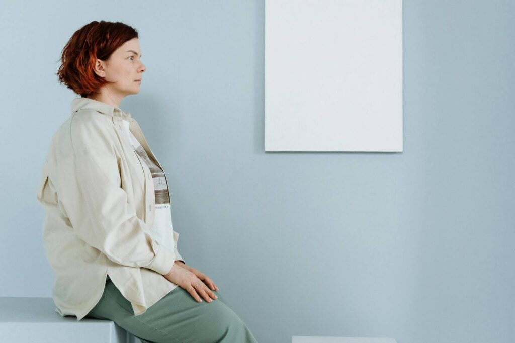 A woman sits on the edge of a table in a doctor's office. She is looking straight ahead with her hands on her lap.