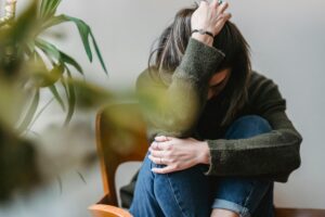 Woman sitting in a chair with her knees drawn up, one hand resting on her knees and the other holding her head, portraying the physical and emotional distress of rebound anxiety from Xanax