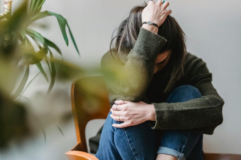 Woman sitting in a chair with her knees drawn up, one hand resting on her knees and the other holding her head, portraying the physical and emotional distress of rebound anxiety from Xanax