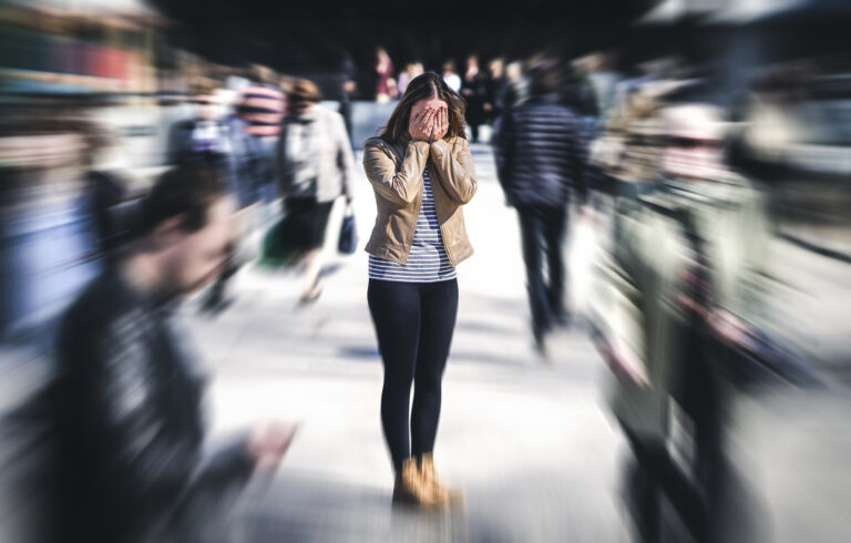 A woman in a crowded outdoor public area struggling with anxiety, deep in thought, wondering how fast does ketamine work for anxiety.